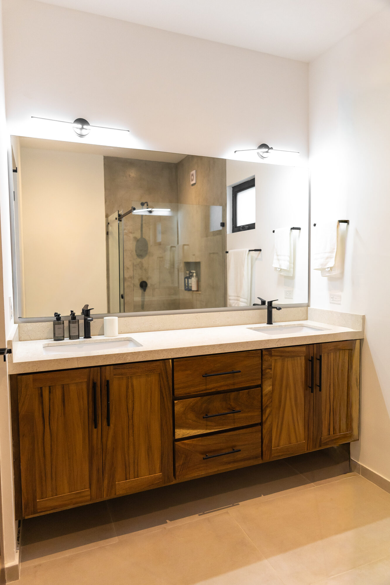 A double-sink bathroom vanity in wood and white stone under a large mirror