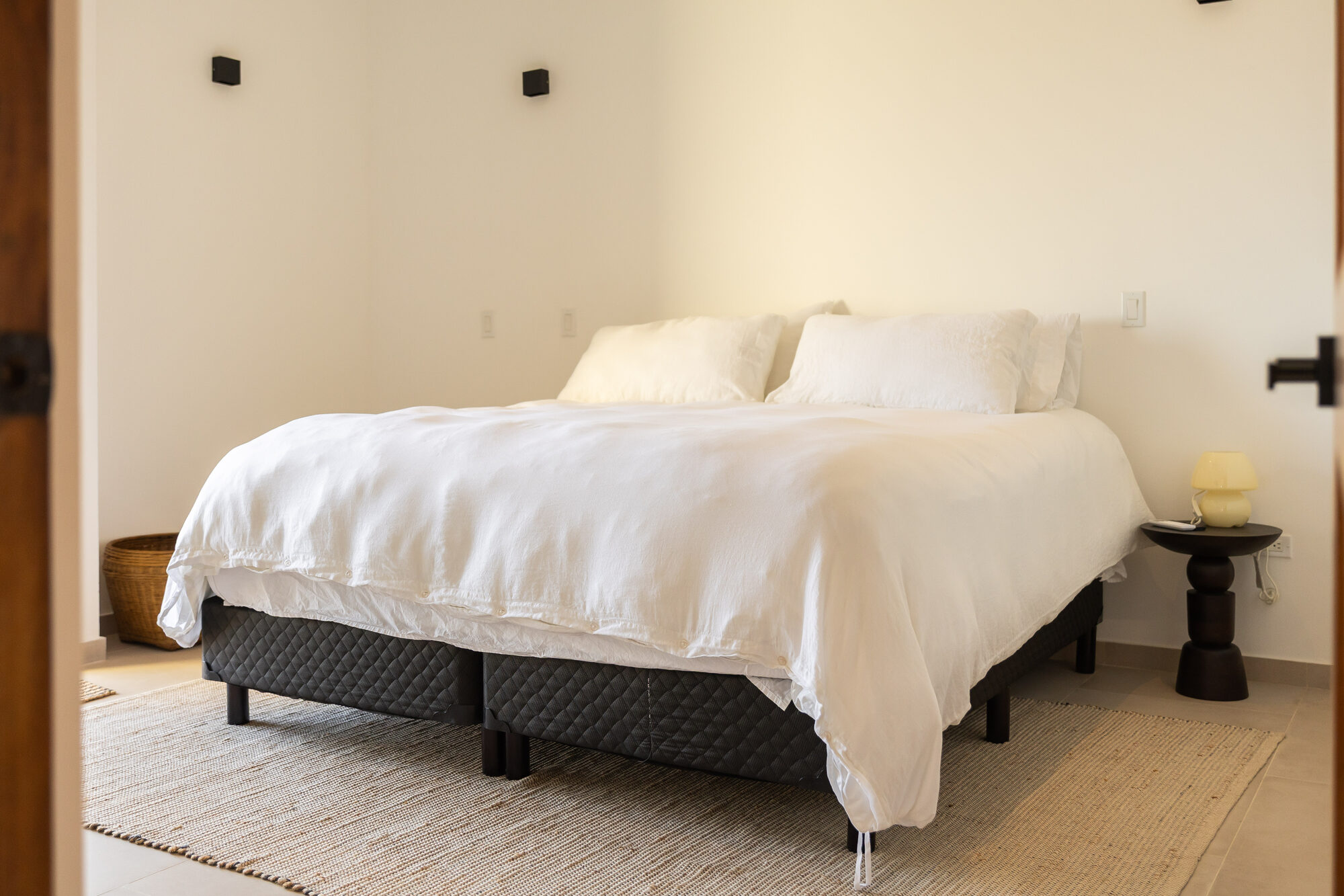 A large bed with white linens and a dark textured base on a woven rug