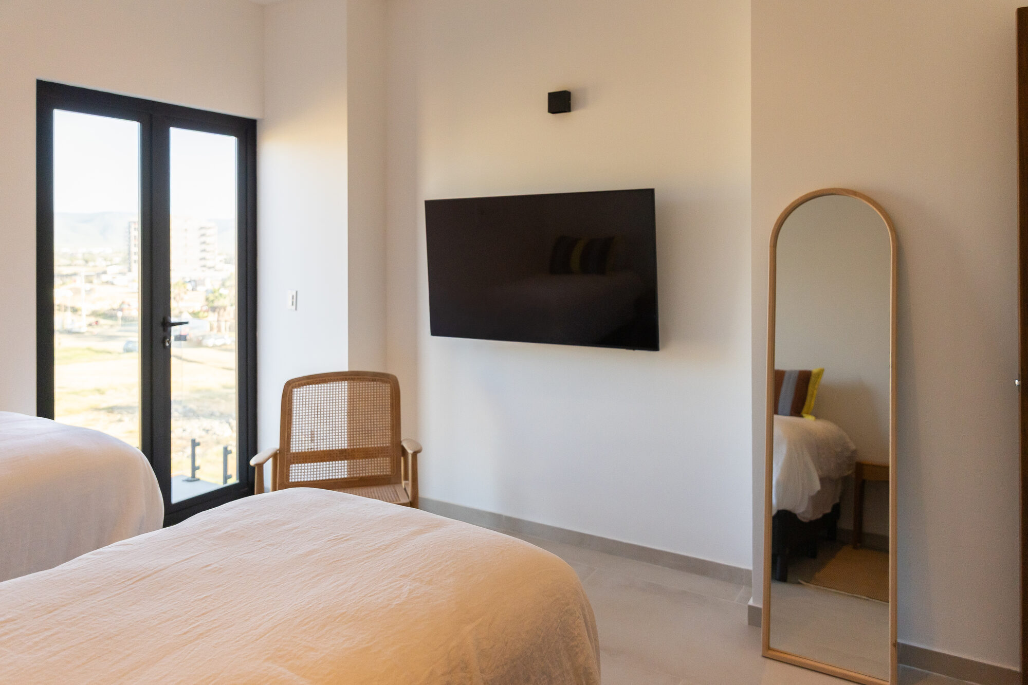 A bedroom with an arched floor mirror and a door to the patio