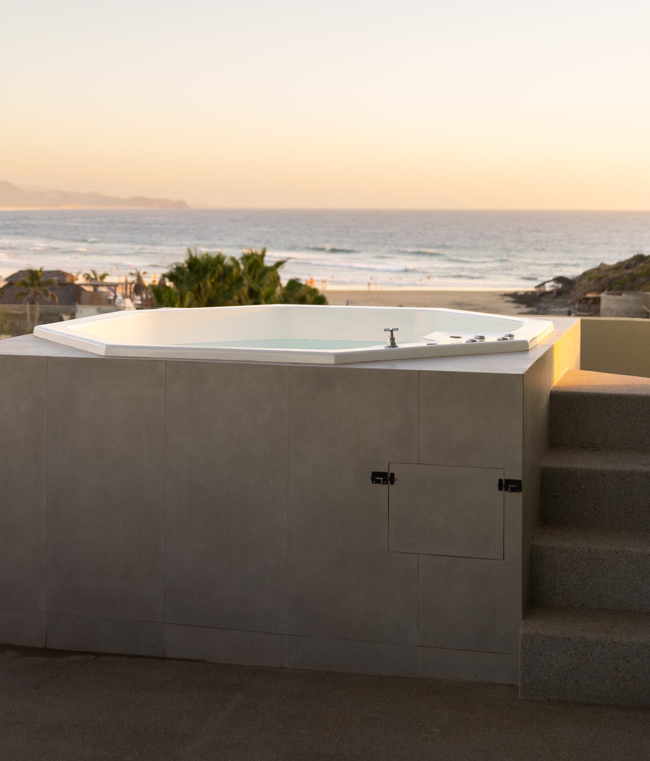 The soaking tub on the private rooftop terrace, string lights above and the beach beyond at sunset